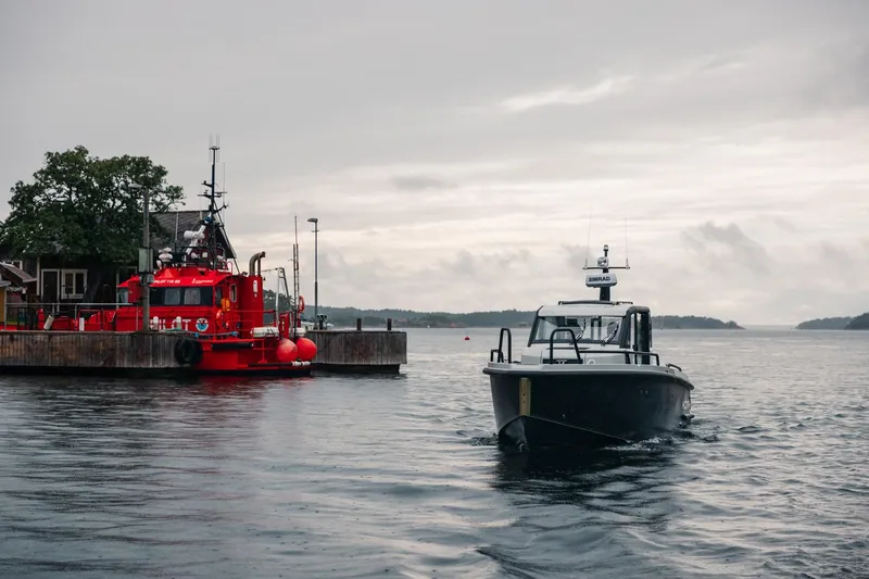 Slide: The Image of Modern XO DFNDR 9 boat on water near red docked vessel, overcast sky. - 12