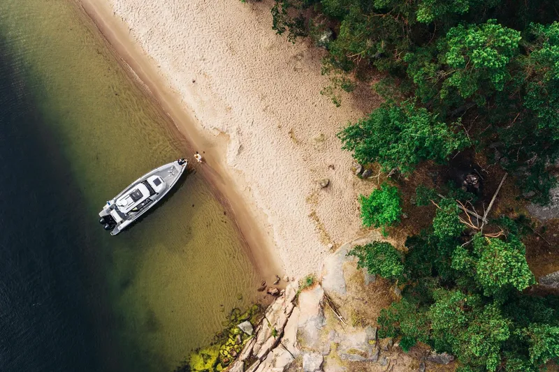 Slide: The Image of Aerial view of XO DFNDR 9 boat on sandy shore, surrounded by lush greenery, 2027 model. - 15