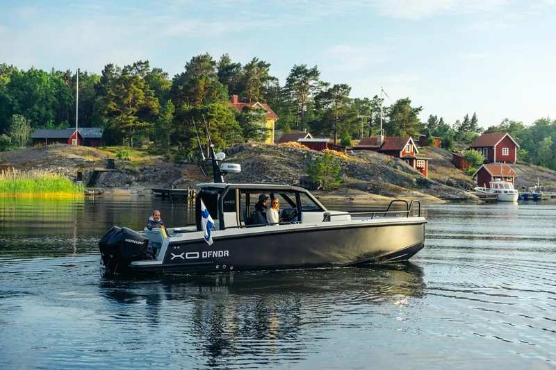 Slide: The Image of 2027 XO DFNDR 9 boat cruising near scenic shoreline with red cottages and lush greenery. - 17