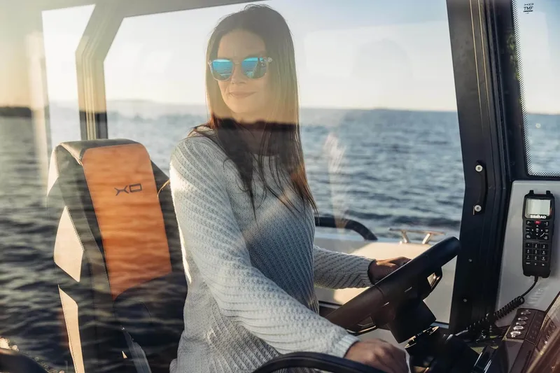 Slide: The Image of Woman piloting 2027 XO DFNDR 9 boat on open water, wearing sunglasses. - 5