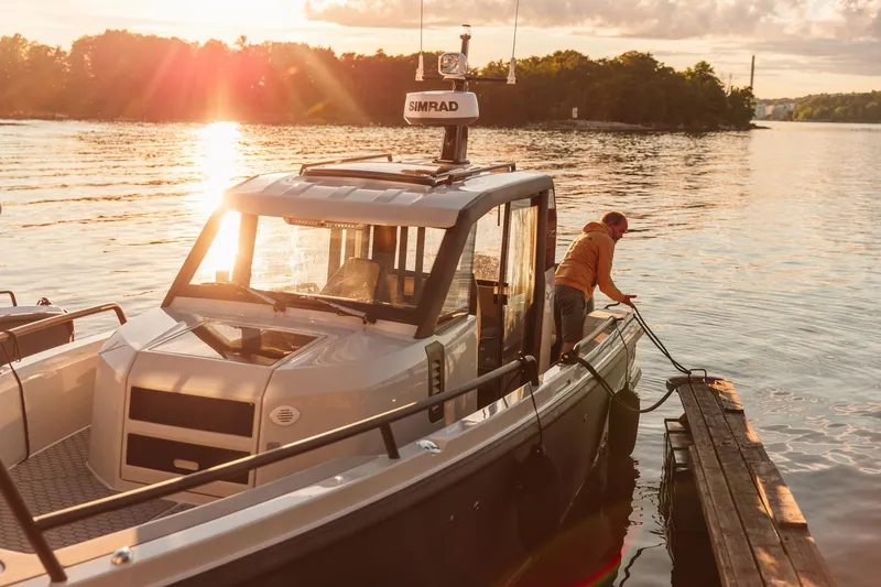 Slide: The Image of 2027 XO DFNDR 9 boat docked at sunset, person securing it to the pier. - 7