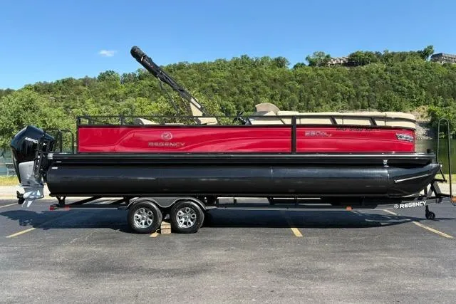 The Image of 2025 Regency 250 DL3 pontoon boat on trailer, red and black design, parked outdoors. - 0