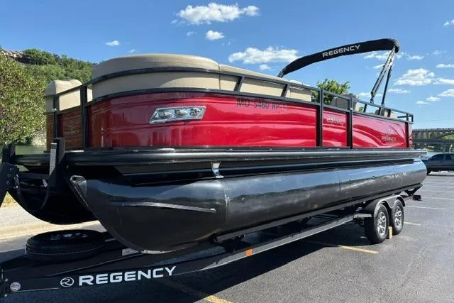 Slide: The Image of 2025 Regency 250 DL3 pontoon boat on trailer, red and black design, sunny day. - 12