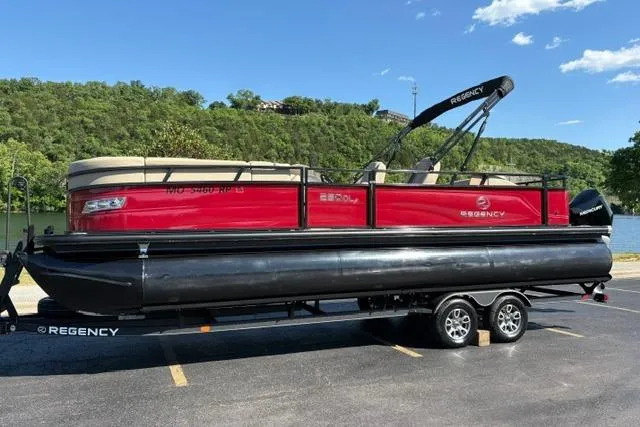 Slide: The Image of 2025 Regency 250 DL3 pontoon boat on trailer, parked near a scenic lake. - 2