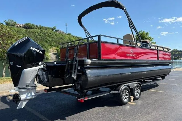 Slide: The Image of 2025 Regency 250 DL3 pontoon boat with Mercury engine on trailer, parked outdoors. - 6