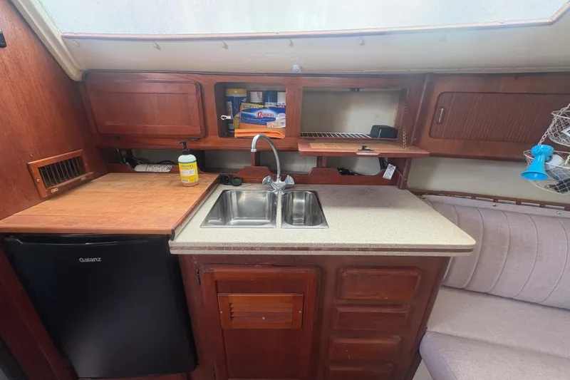 Slide: The Image of 1989 Hunter Vision 32 yacht interior kitchen with sink, wooden cabinets, and compact fridge. - 59