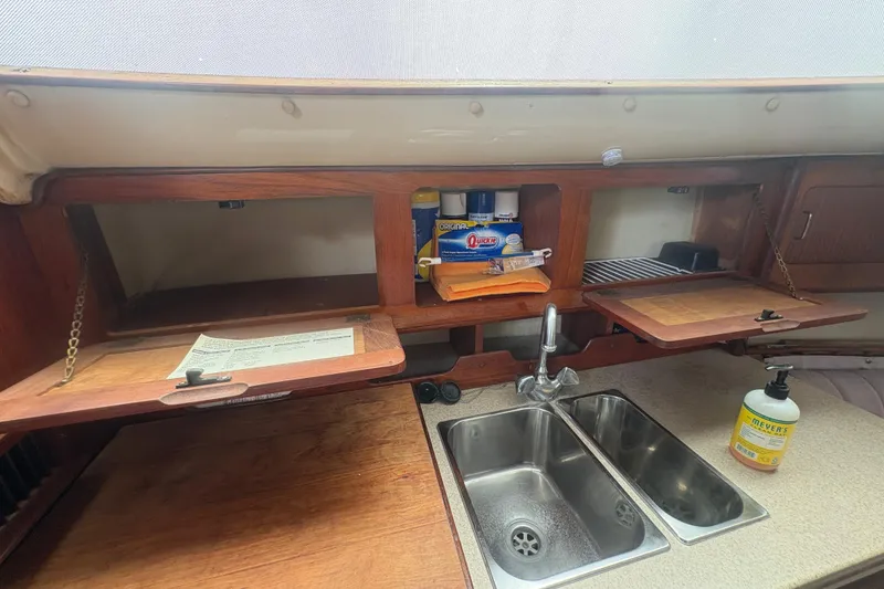 Slide: The Image of 1989 Hunter Vision 32 yacht kitchen with wooden cabinets, dual sink, and cleaning supplies. - 60