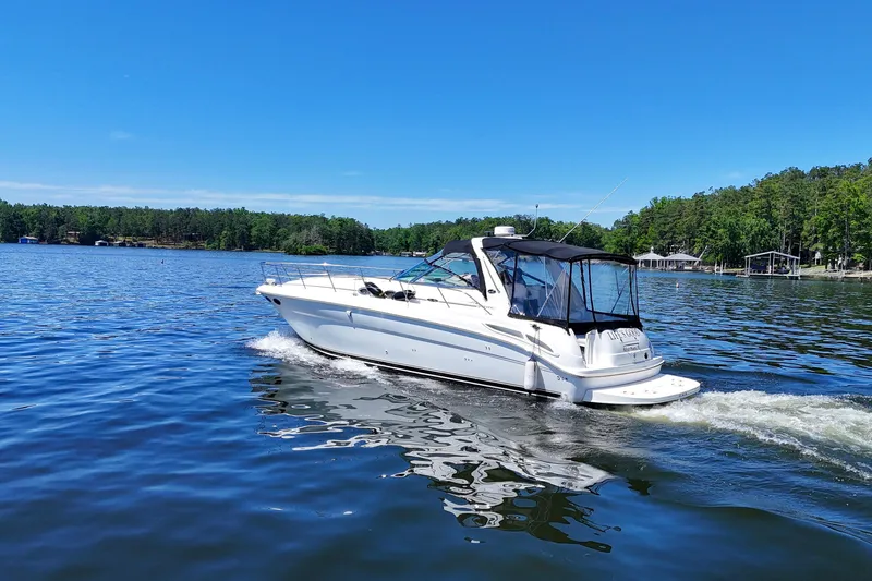 Slide: The Image of 2003 Sea Ray 380 Sundancer cruising on a serene lake under a clear blue sky. - 14