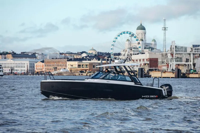 Slide: The Image of 2027 XO DSCVR 9 T-TOP boat cruising in urban waterfront setting with cityscape backdrop. - 9