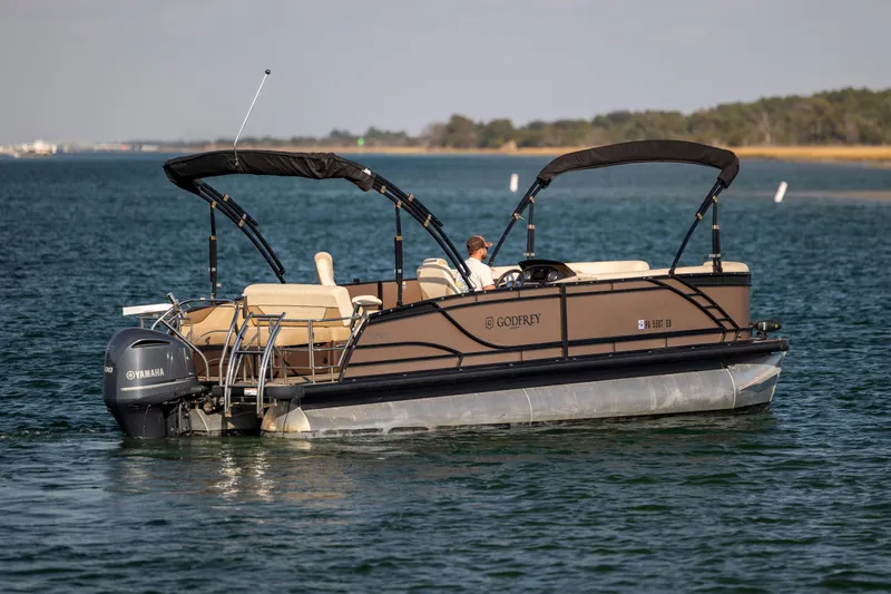 Slide: The Image of 2022 Godfrey Monaco 255 SFL pontoon boat cruising on a serene lake. - 7