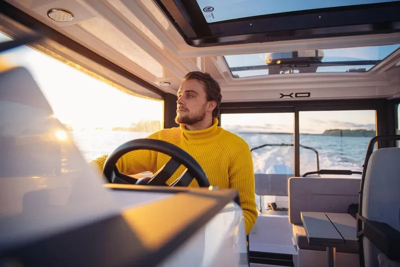 Slide: The Image of Man steering XO EXPLR 9 boat, 2027 model, during sunset on open water. - 14