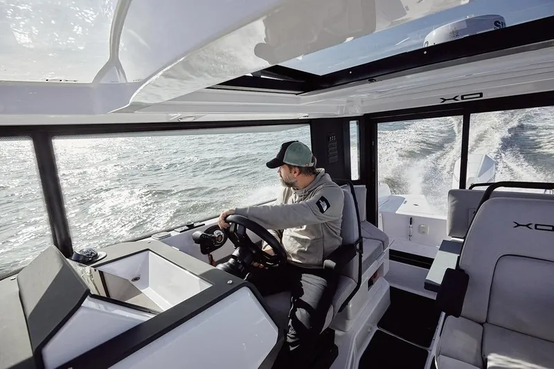 Slide: The Image of Man steering 2027 XO EXPLR 9 boat on open water, interior view. - 2