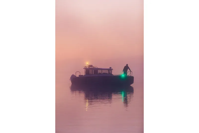 Slide: The Image of Silhouetted XO EXPLR 9 boat on misty water at sunset, 2027 model. - 4