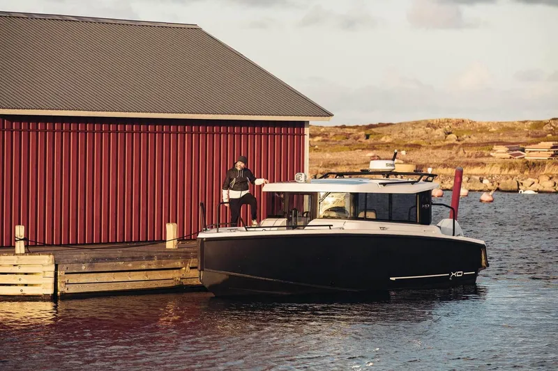 Slide: The Image of Modern XO EXPLR 9 boat docked beside a red boathouse, scenic coastal backdrop. - 7