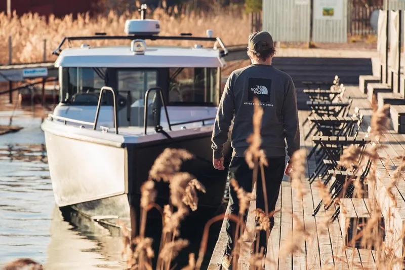 Slide: The Image of Man walking on dock beside 2027 XO EXPLR 9 boat, surrounded by reeds. - 9