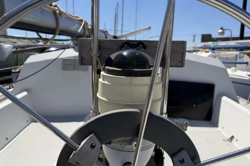 Slide: The Image of 1988 O'Day 302 sailboat cockpit with steering wheel and compass, docked under clear sky. - 12