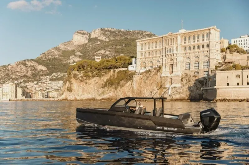 Slide: The Image of Modern XO DFNDR A8 boat cruising near a scenic coastal cliff and historic building, 2027 model. - 1