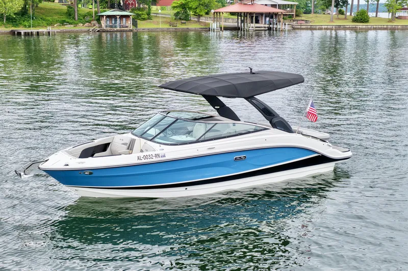 Slide: The Image of 2023 Sea Ray SLX 260 boat with blue hull, black canopy, and American flag on a serene lake. - 2