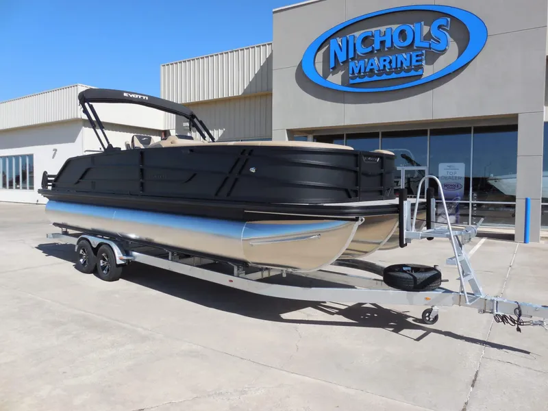 The Image of The image shows a 2027 Evotti 525CS pontoon boat on a trailer in front of a building. - 0