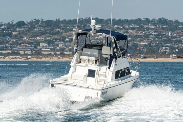 Slide: The Image of 2011 Skipjack 300 Flybridge boat cruising on water near coastal town. - 16