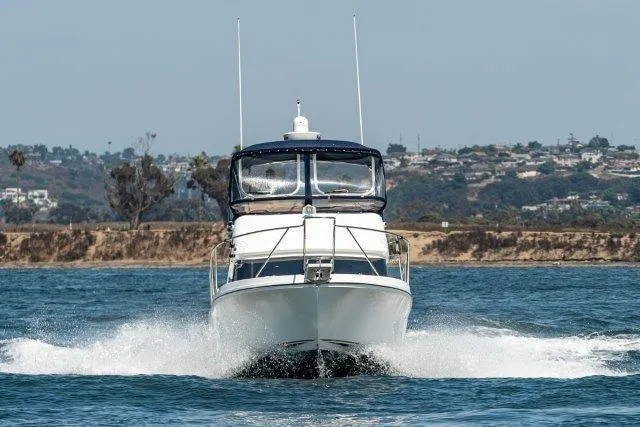 Slide: The Image of 2011 Skipjack 300 Flybridge cruising on open water with scenic shoreline backdrop. - 8
