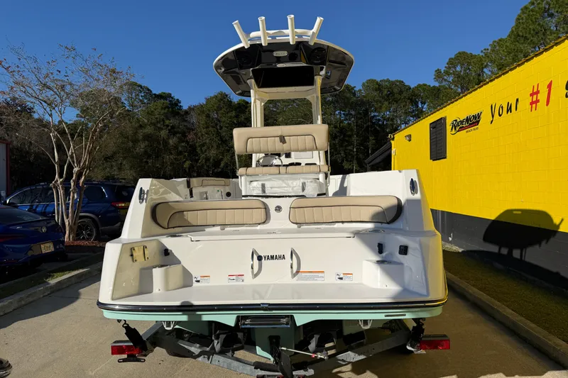 Slide: The Image of 2026 Yamaha Boats 222 FSH Sport E, rear view, parked outdoors near a yellow building. - 10