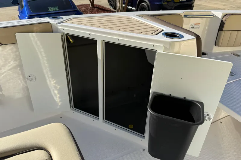 Slide: The Image of 2026 Yamaha Boats 222 FSH Sport E interior storage compartment with open doors and trash bin. - 29