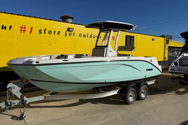 Slide: The Image of 2026 Yamaha Boats 222 FSH Sport E on trailer, parked by a yellow building. - 3