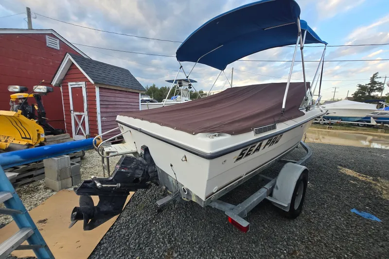 Slide: The Image of 1994 Sea Pro 190 Dual Console boat on trailer, covered, with blue canopy, near red shed. - 4