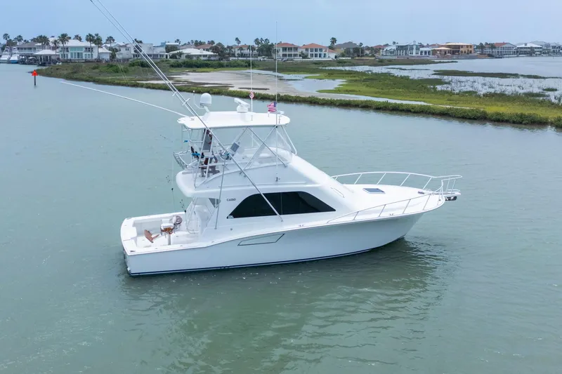 The Image of 2005 Cabo 40 Flybridge yacht cruising in calm waters near coastal homes. - 0