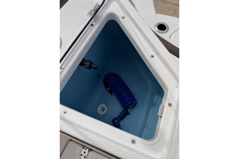 Slide: The Image of 2026 Yamaha Boats 222 FSH Sport storage compartment with blue coiled hose. - 18
