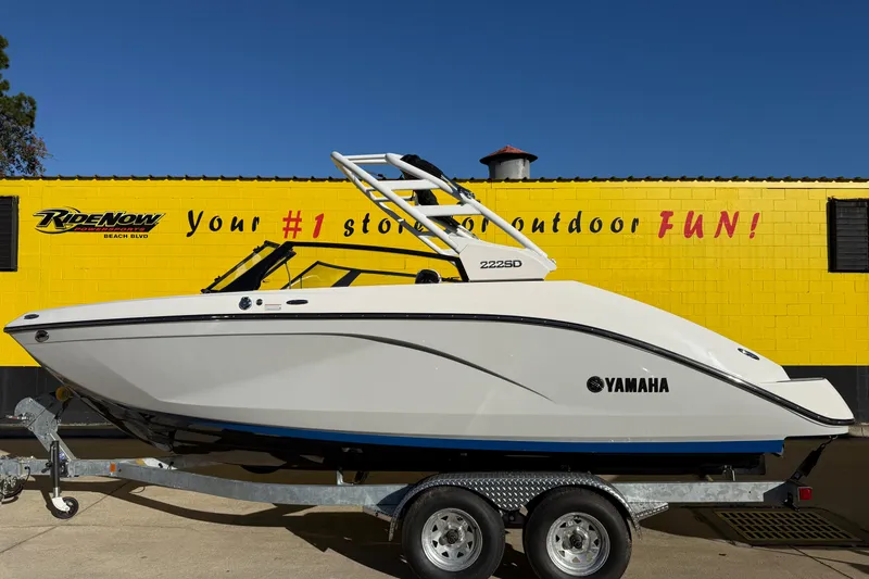 The Image of 2026 Yamaha Boats 222SD on trailer, parked outside a yellow building with promotional signage. - 0