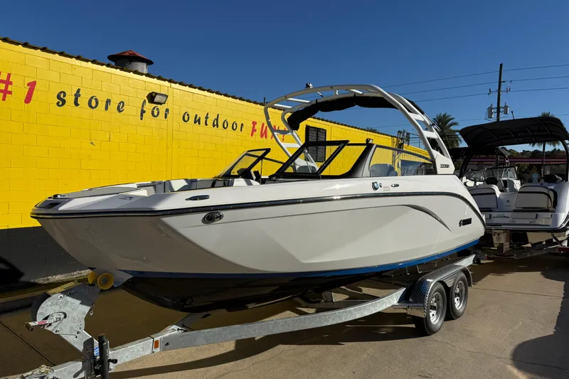 Slide: The Image of 2026 Yamaha Boats 222SD on trailer, parked outside a yellow building under clear blue sky. - 3