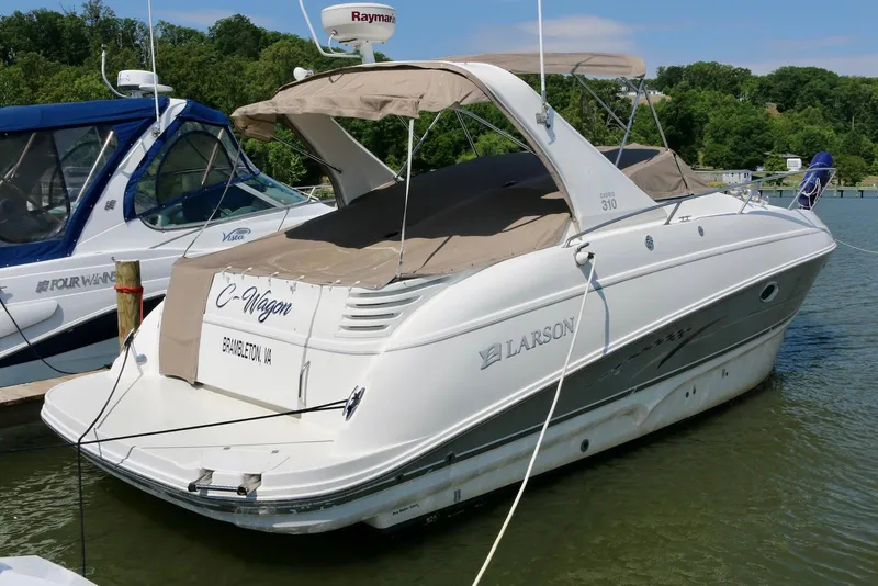 Slide: The Image of 2009 Larson Cabrio 310 boat docked in a marina, featuring a beige canopy. - 3