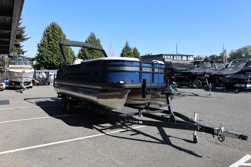Slide: The Image of 2026 Lowe SS 230 CL pontoon boat on trailer in parking lot, surrounded by trees and other boats. - 10