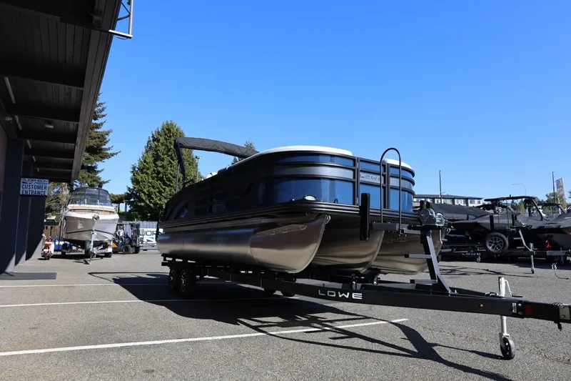Slide: The Image of 2026 Lowe SS 230 CL pontoon boat on trailer in parking lot under clear blue sky. - 11