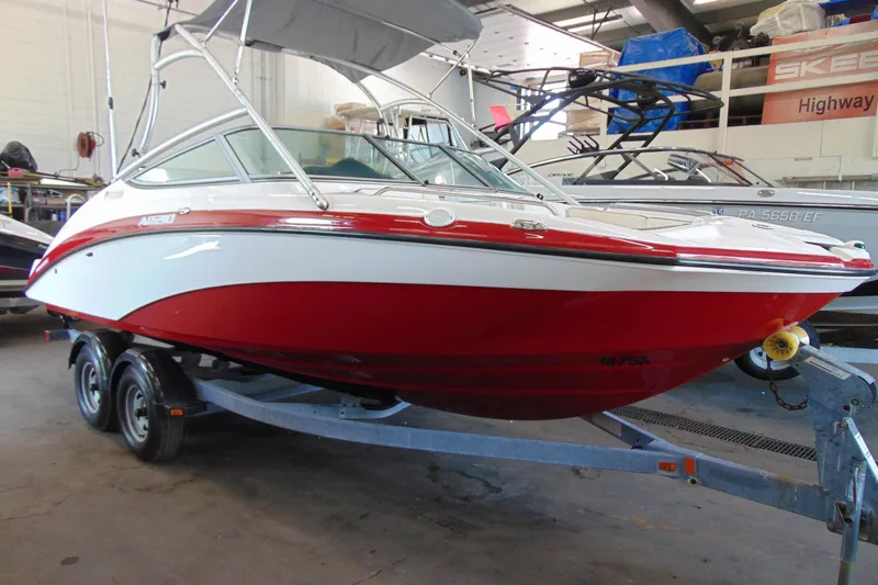 The Image of 2014 Yamaha Boats AR210 in a showroom, red and white design on trailer. - 2