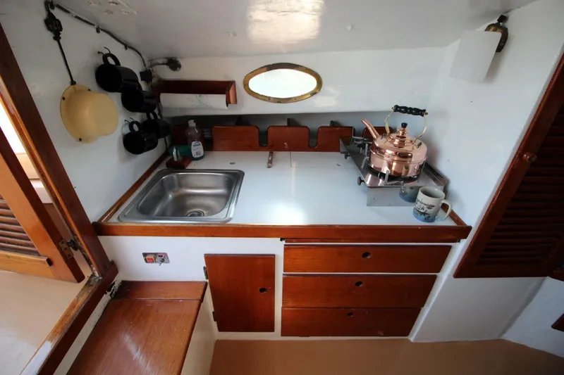 Slide: The Image of 1974 Marshall 22 Cape Cod Catboat galley with sink, stove, and wooden cabinetry. - 16