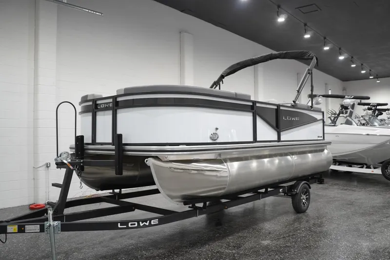 Slide: The Image of 2026 Lowe LS 190 pontoon boat on trailer in showroom setting. - 11