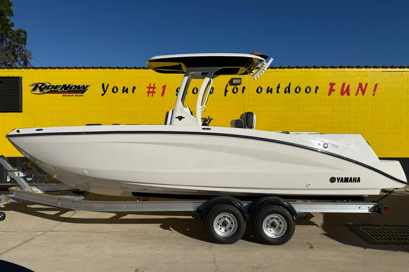 The Image of 2026 Yamaha Boats 252 FSH Sport on trailer, parked by yellow building. - 1
