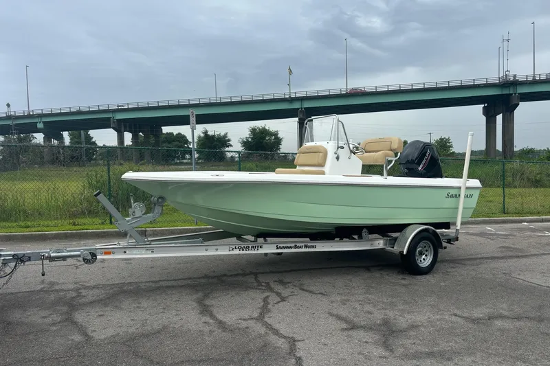 Slide: The Image of 2025 Savannah 190 IS boat on trailer, parked near a bridge on a cloudy day. - 6