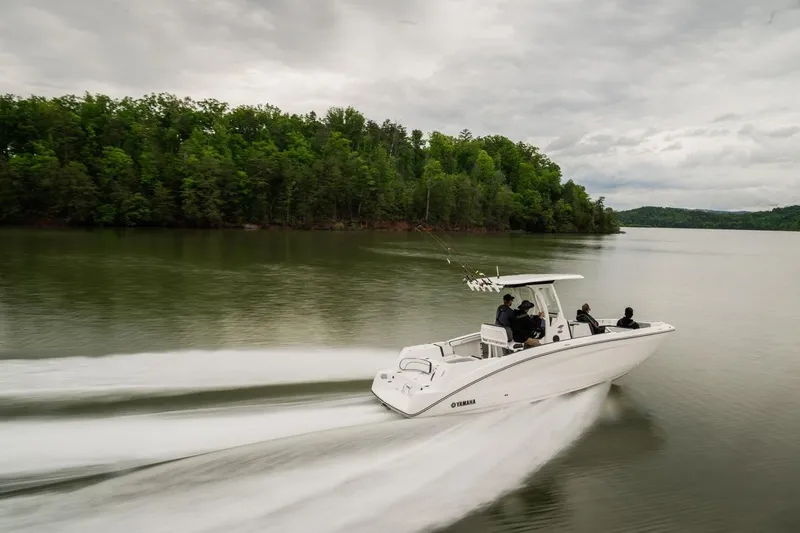 Slide: The Image of 2026 Yamaha Boats 252 FSH Sport cruising on a serene lake with lush green shoreline. - 10