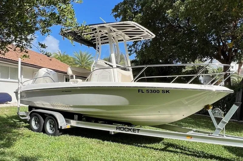 The Image of 2019 Boston Whaler 210 Dauntless boat on trailer, parked on grass under blue sky. - 0