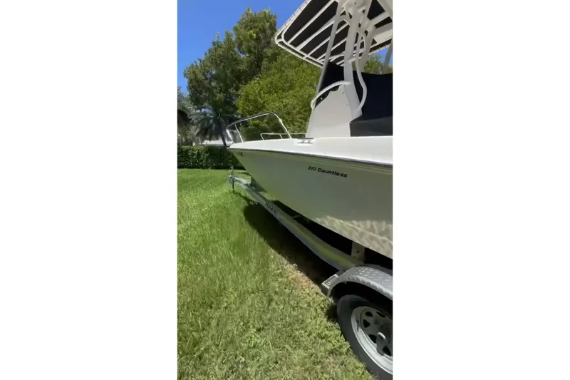 Slide: The Image of 2019 Boston Whaler 210 Dauntless boat on trailer, parked on grass. - 2