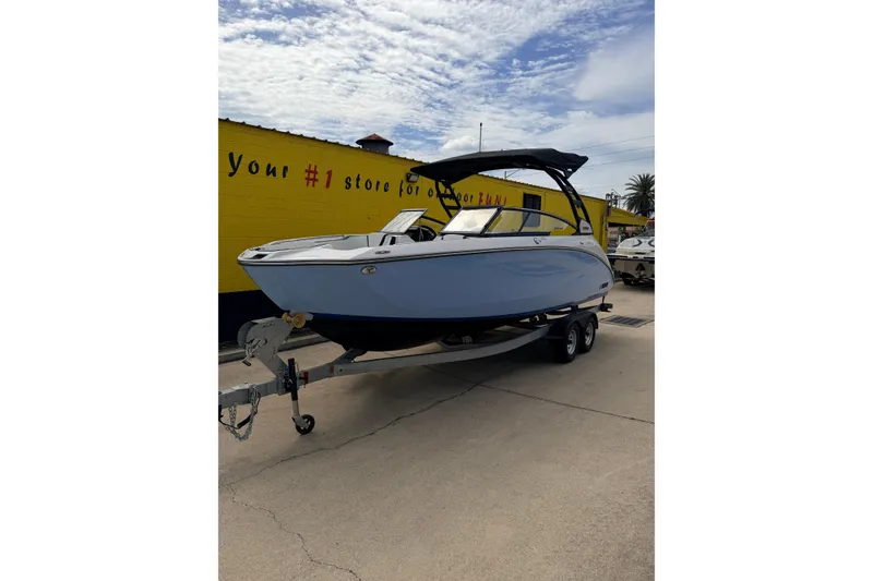 The Image of 2026 Yamaha Boats 252SD on trailer, parked outside a yellow building under a cloudy sky. - 0