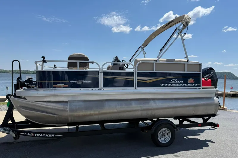 The Image of 2023 Sun Tracker Bass Buggy 16 XL Select pontoon boat on trailer by a lake. - 1