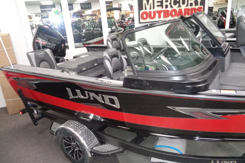 Slide: The Image of 2026 Lund 1875 Pro-V boat displayed indoors, featuring sleek design and Mercury outboard motor. - 2