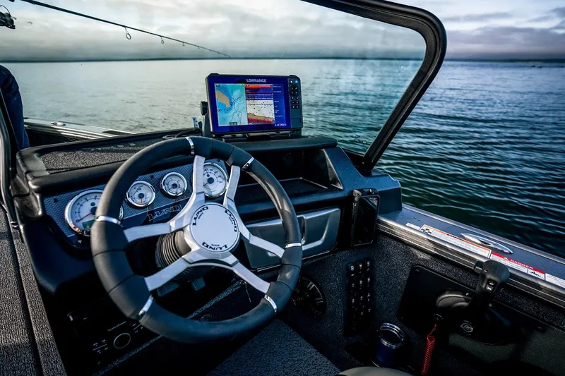 Slide: The Image of Manufacturer Provided Image: 2025 Lund 1875 Pro-V boat dashboard with steering wheel and navigation system on a calm lake. - 21