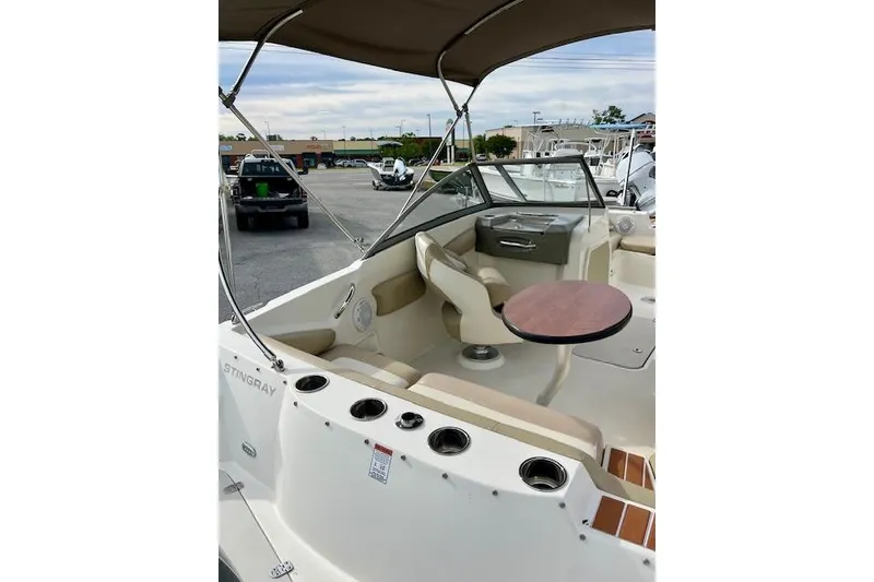 Slide: The Image of 2019 Stingray 201 DS boat interior with seating, table, and canopy in a parking lot. - 5