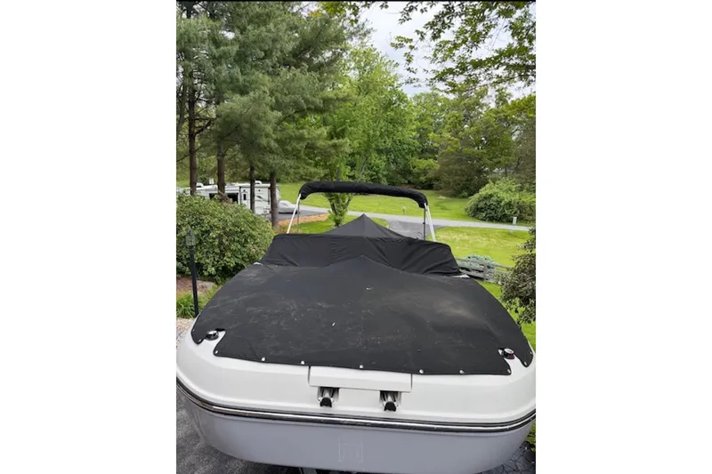 Slide: The Image of 2023 Bayliner DX 2200 boat covered, parked outdoors amidst lush greenery. - 14